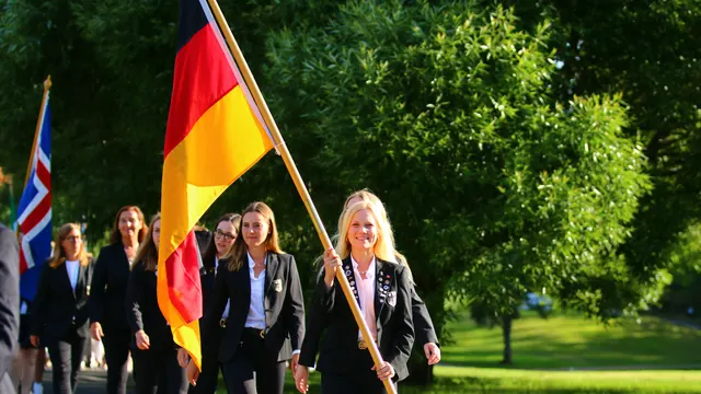Nationalmannschaft in dunklen Blazern beim Einmarsch, eine Spielerin trägt die Deutschlandfahne