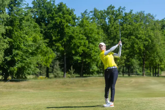 Celina Sattelkau: Eisenschlag vom Fairway im gelben Oberteil vor dichten Bäumen