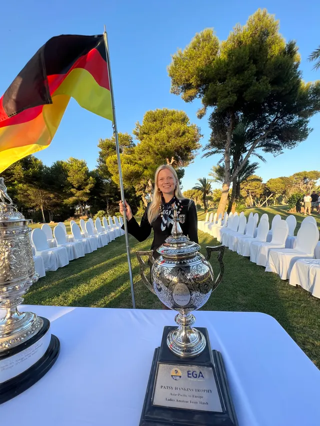 Celina Sattelkau: mit Deutschlandfahne neben großem Silberpokal in der Stuhlreihe der Siegerehrung
