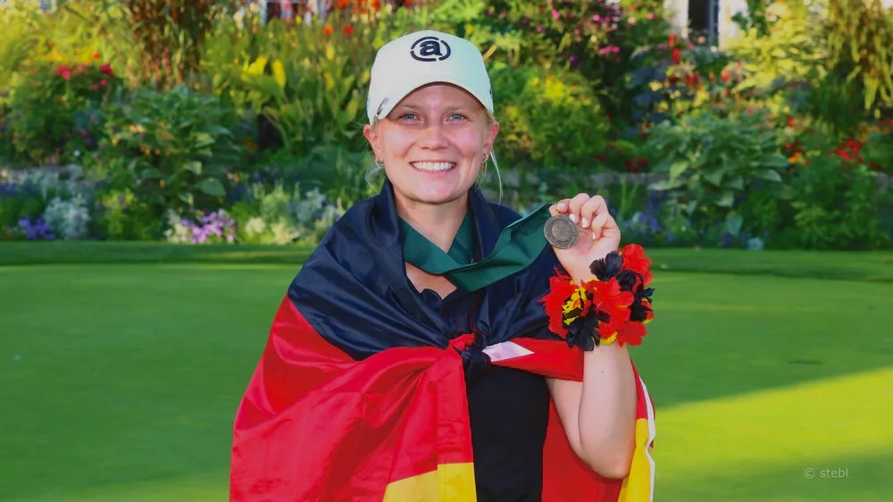 Celina Sattelkau: mit Deutschlandfahne um die Schultern zeigt lachend ihre Medaille