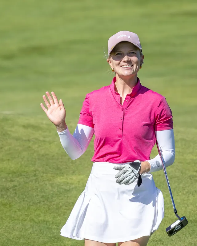 Celina Sattelkau: winkt lächelnd mit Sonnenbrille und pinkem Polo, Handschuh und Putter in der Hand