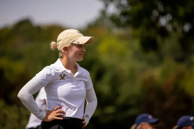 Celina Sattelkau: Porträt mit Hand in der Hüfte, weißes Vanderbilt-Polo, helle Cap, unscharfes Grün