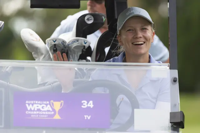 Celina Sattelkau: Lacht im Golfcart neben Schlägerbag, schwarzes Cap, Turnierschilder